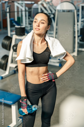 Lifestyle portrait of a smiling young sporty woman with blue water bottle in a fitness studio