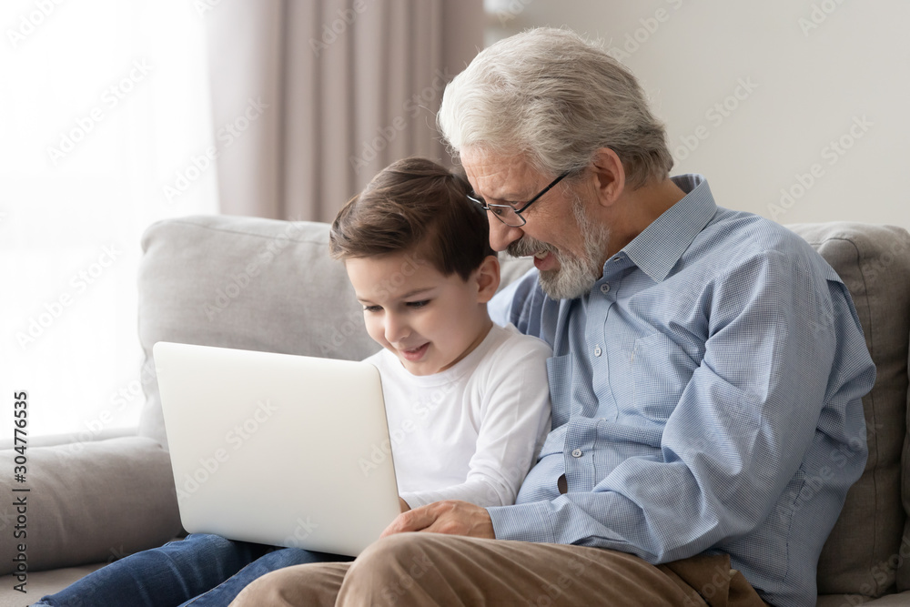 Happy grandfather and cute little grandson using laptop together