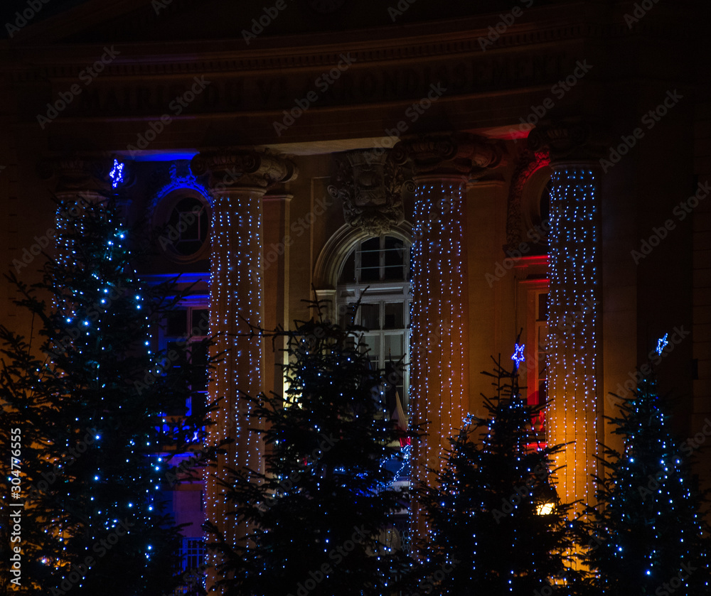 Christmas in Paris, France. Christmas tree decorated with light garlands and a building illuminated with colors of French flag at background.
