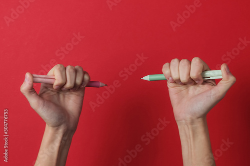 Ambidextr. Female hands hold pens on a red background. Top view. Studio shot
