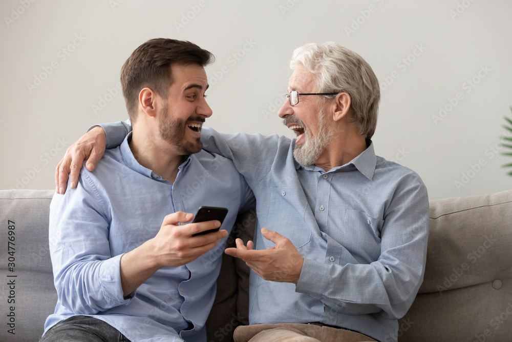Happy old father and son having fun, using phone together - obrazy, fototapety, plakaty 