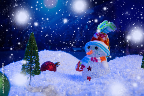 Snowman with Christmas balls on snow over fir-tree  night sky and moon. Shallow depth of field. Christmas background. Fairy tale. Macro. Artificial magic dreamy world.