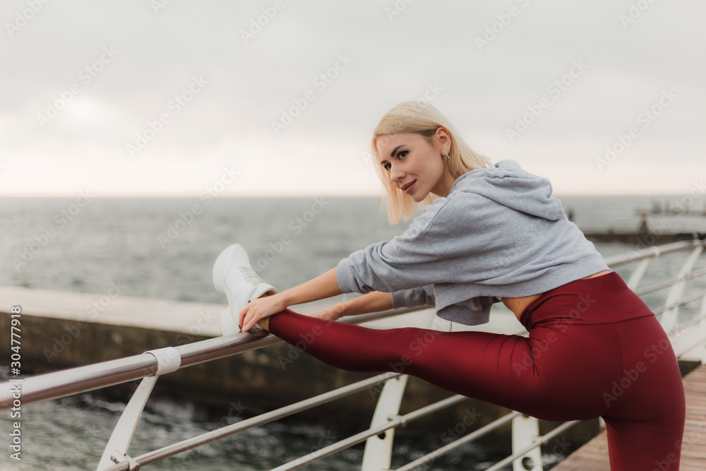 Morning workout. Healthy lifestyle concept. Young attractive woman in sportswear does leg stretching before exercise on the beach at sunrise. Warm up