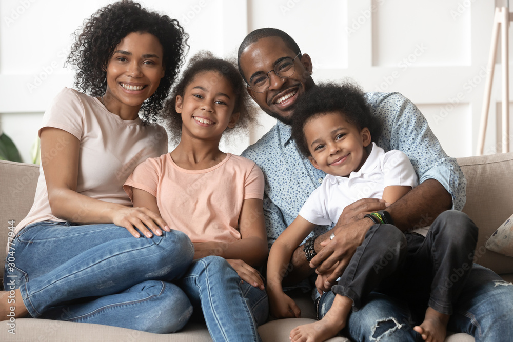 African couple little kids sitting on couch looking at camera African couple little kids sitting on couch looking at camera