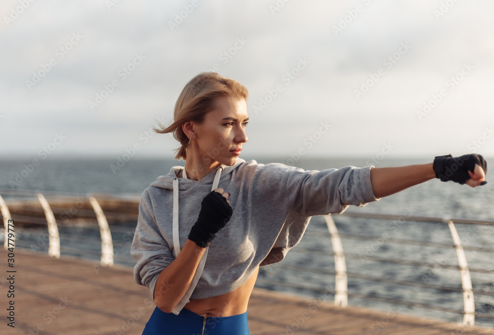 Young woman kickboxer with wrapped hands in bandages trains punch on the beach at sunrise. Morning training fighter Young woman kickboxer with wrapped hands in bandages trains punch on the beach at sunrise. Morning training fighter