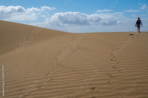 Person is walking on sand dunes during sunny and windy day in the Natural Reserve of Dunes of Maspaloma in Gran Canaria with sand dust  and foot steps. Canary Islands  Spain
