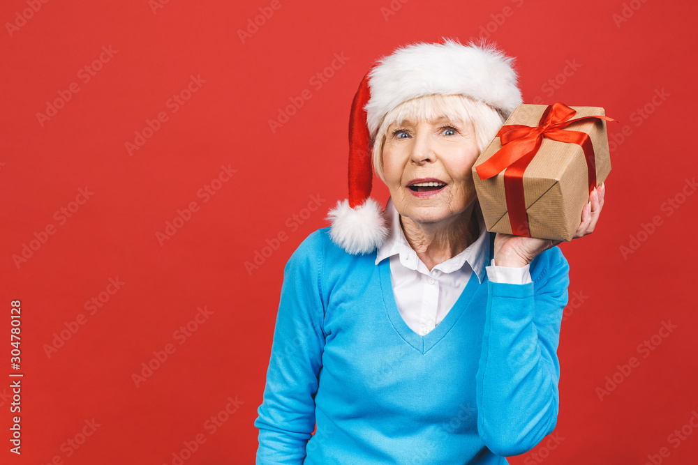 Happy mature woman with a gift. Isolated over red background. Beautiful stylish senior lady opening her Christmas gift. Elegant mature woman holding a red gift box. Happy mature woman with a gift. Isolated over red background. Beautiful stylish senior lady opening her Christmas gift. Elegant mature woman holding a red gift box.