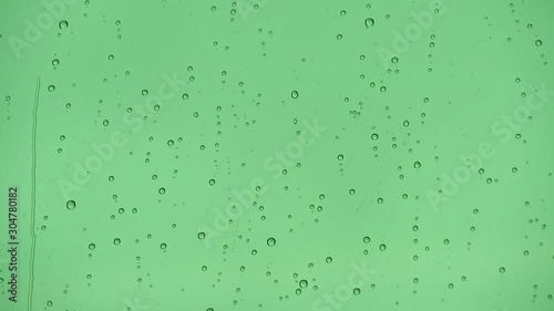 Close up view of water drops falling on green color window glass.