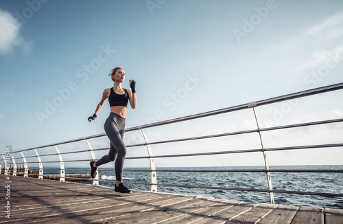 Fototapeta Naklejka Na Ścianę i Meble -  Morning run. Young athletic woman in sportswear runs on the beach at sunrise. Outdoor workout. Healthy lifestyle