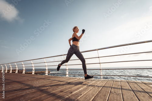 Morning run. Young athletic woman in sportswear runs on the beach at sunrise. Outdoor workout. Healthy lifestyle