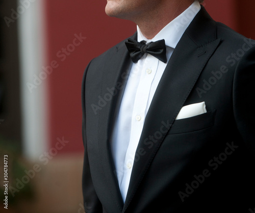 man with tuxedo in motion white shirt black bow tie black jacket and white scarf background in green and terracotta colors