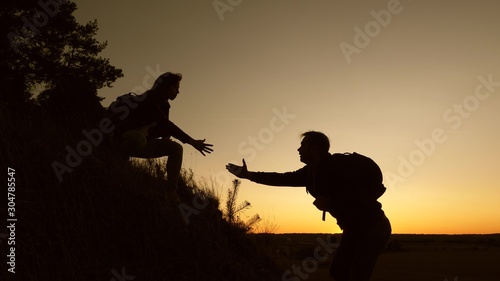 work in a team of climbers. female traveler holds the hand of a male traveler helping to climb top of hill. Tourists climb mountain at sunset, holding hands. team work of business partners.