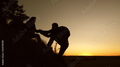 work in a team of climbers. female traveler holds the hand of a male traveler helping to climb top of hill. Tourists climb mountain at sunset, holding hands. team work of business partners.