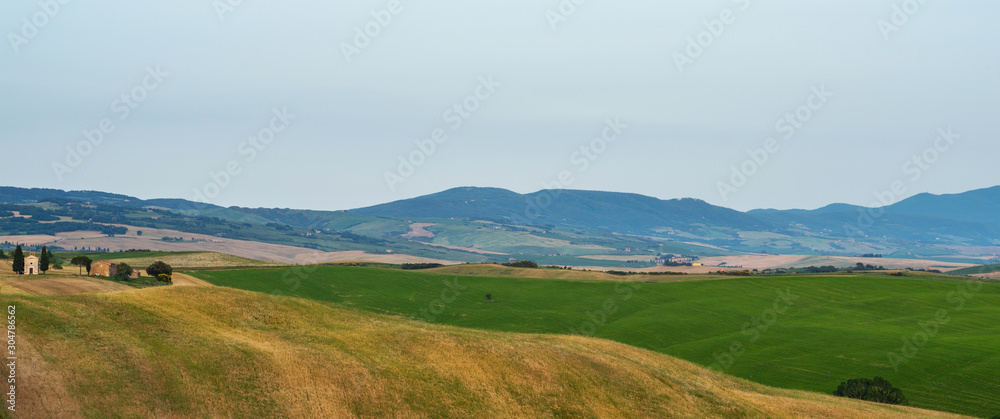 Obraz premium View of a sunny day in the Italian rural landscape. Unique Tuscany landscape in summer time. Wave hills, colorful fields, cypresses trees and sky.