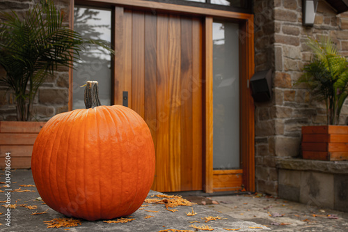 Large pumpkin standing at the front doors outside of the fancy home. Season outdoor decoration for the halloween in USA and Canada.
