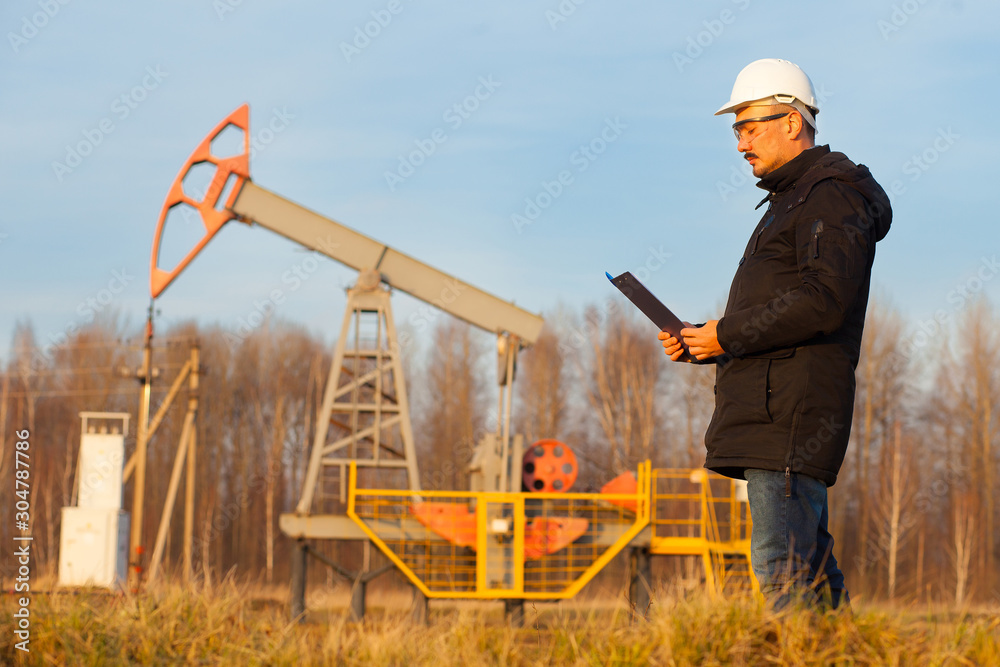 Engineer in a white helmet on an oil rig with a tablet. Oil production in Russia, Republic of Bashkortostan. Quality control. Oil production schedule Engineer in a white helmet on an oil rig with a tablet. Oil production in Russia, Republic of Bashkortostan. Quality control. Oil production schedule
