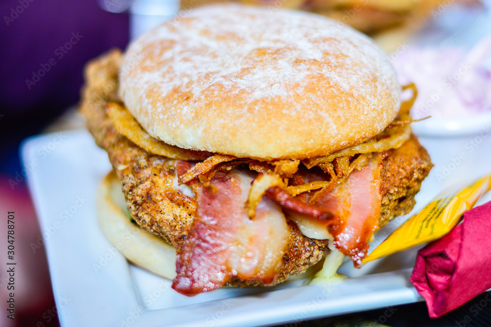 Closeup of Burger with Chicken, Bacon and Fried Onions on White Plate