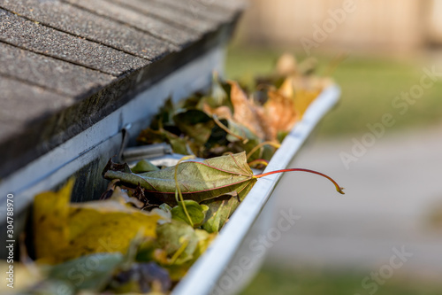 Closeup of house rain gutter clogged with colorful leaves fall from trees in fall. Concept of home maintenance and repair photo