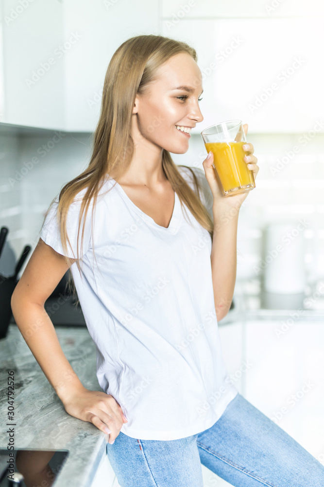 Attractive young woman holding a glass of orange juice while standing in the kitchen Attractive young woman holding a glass of orange juice while standing in the kitchen