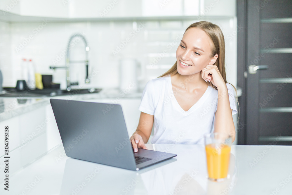 Young beautiful woman using laptop computer in the kitchen Young beautiful woman using laptop computer in the kitchen