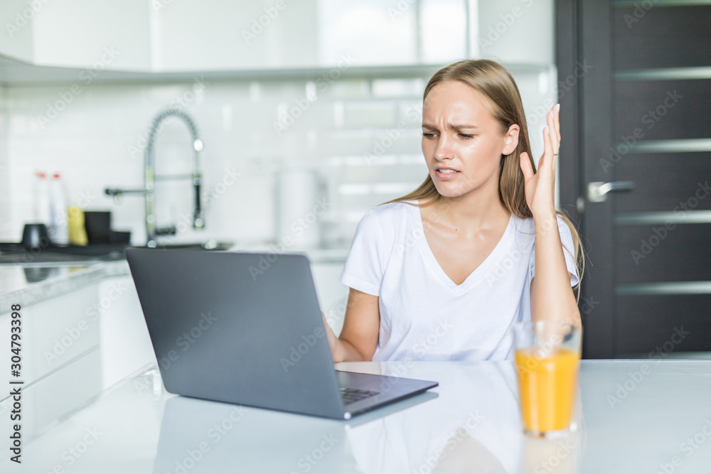 Young woman having headache while working on laptop sitting at her kitchen table at home. Young woman having headache while working on laptop sitting at her kitchen table at home.