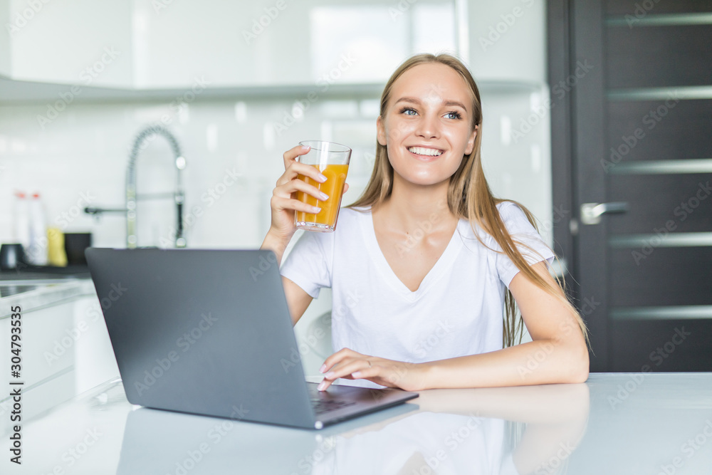 Attractive young woman using laptop and sitting in the kitchen Attractive young woman using laptop and sitting in the kitchen