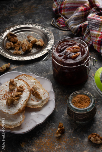 Jar of homemade plum jam marmalade with walnuts and french bread on the kitchen dark table. Healthy dessert snack recipes concept. 
