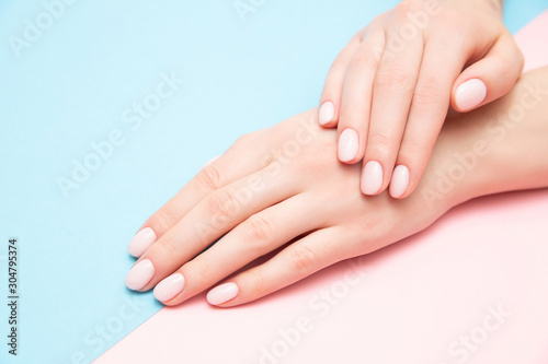 Beautiful female hands with stylish nail manicure gel polish on pink and blue background  top view. Skin care concept