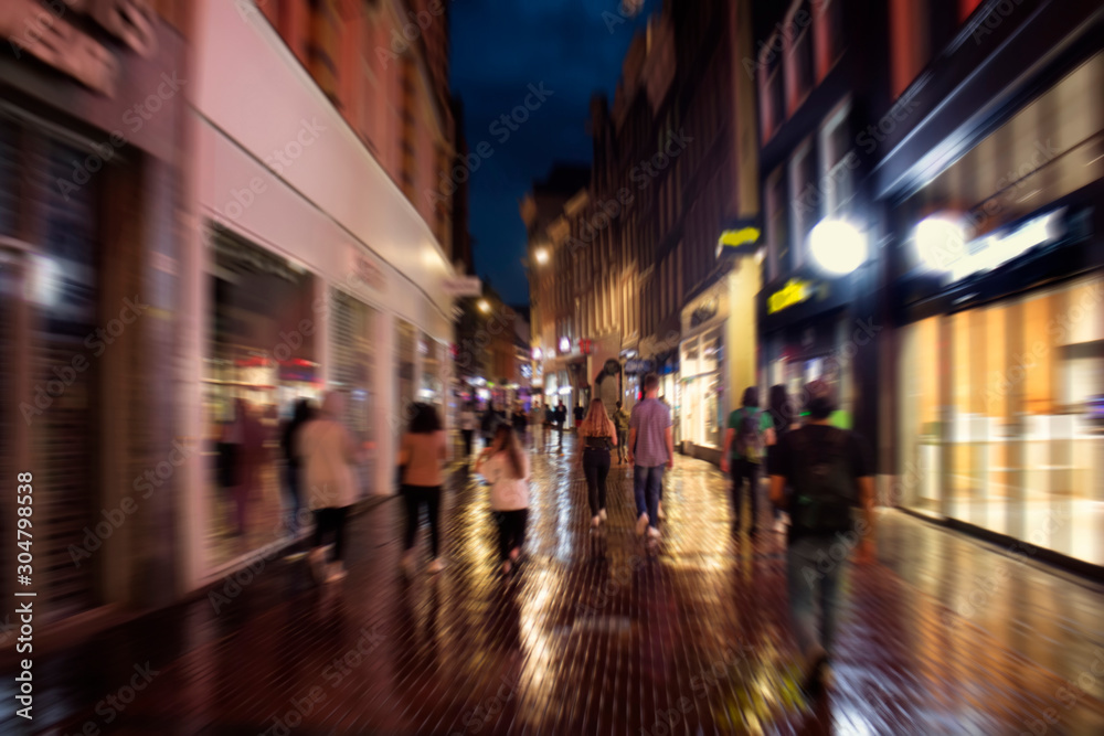Blurry motion image of young people walking on Kalverstraat street which is one of the main shopping streets in Amsterdam. It is a rainy summer night. Youth culture concept.