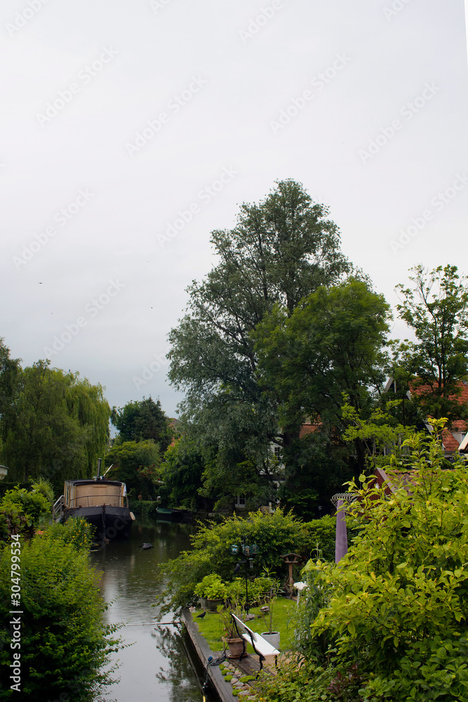 View of canal, trees, bench, plants in Edam. It is a town famous for its semi hard cheese in the northwest Netherlands, in the province of North Holland.