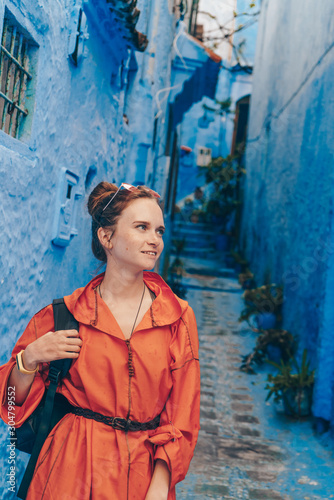 a tourist in an orange dress is standing in the narrow street of the blue city of morocco © nelen.ru