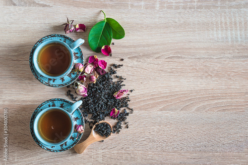 Tea time concept. Two chinese cups of tea, dry tea, rose buds and petals on the wooden background. Flat lay, copy space