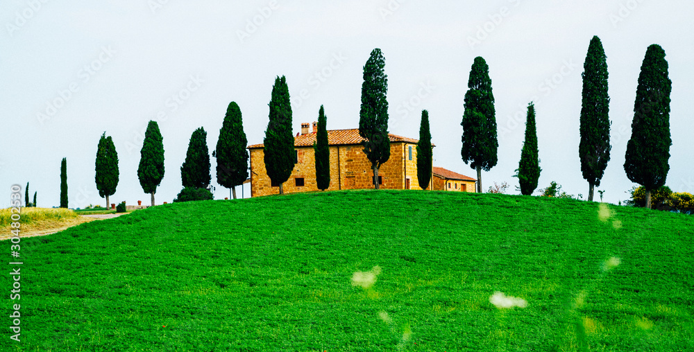 Tuscany beautiful spring landscape. Agricultural area with fields and farmhouse. Countryside farm, cypresses trees, green field, sun light and cloud, Italy, Europe.