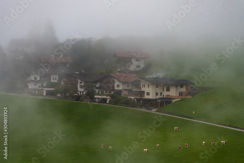 Mountain village Alps Tirol with individual clouds and fog fields. Green fields with some warm light taken with the telephoto lens
