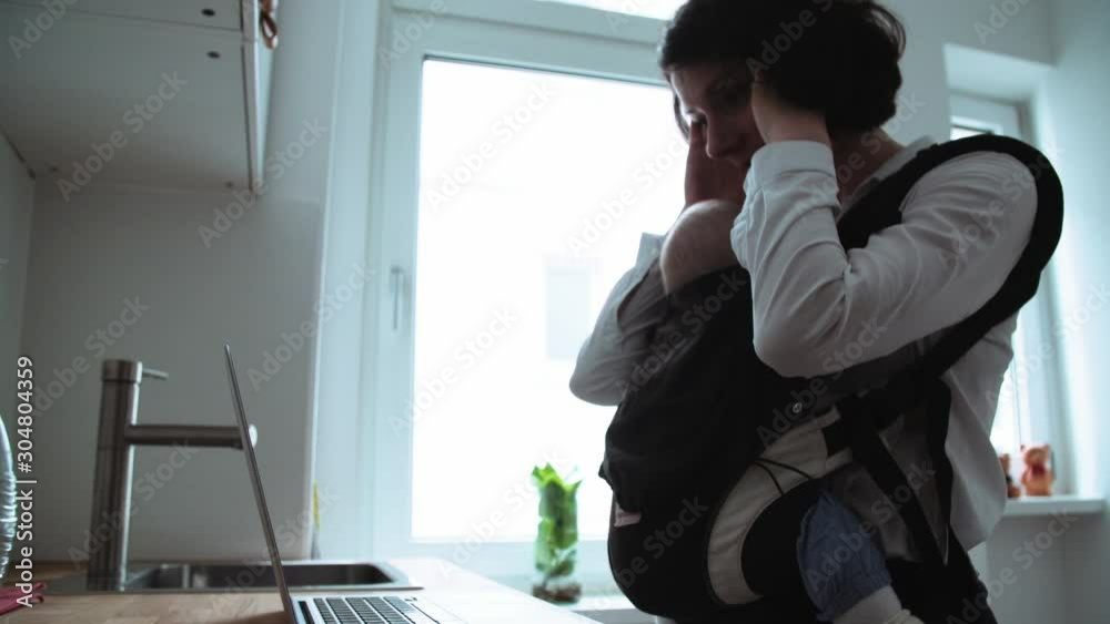 Mother Working from Home on Computer with Baby Sleeping in Sling