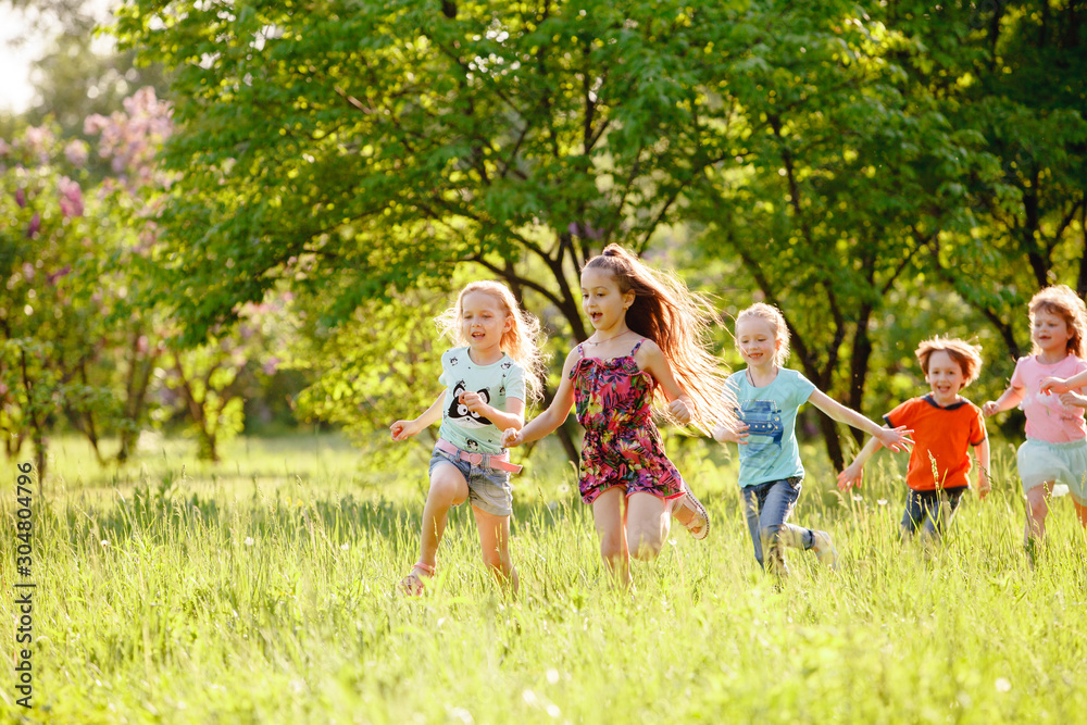 Obraz premium A group of happy children of boys and girls run in the Park on the grass on a Sunny summer day . The concept of ethnic friendship, peace, kindness, childhood