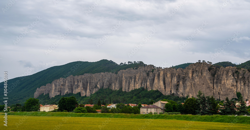 Beautiful stone cliffs above town. Rural houses located in valley surrounded by hills with rocky cliffs in Alpes de Haute Provence, France.