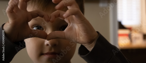Small baby boy holding his hands with the heart-shape figure and looking through it.close up