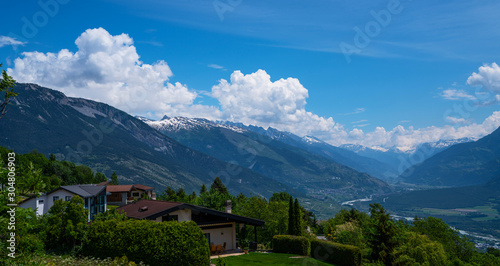 Stunning alpine panorama colorful summer view. Beautiful outdoor scene Switzerland, Europe. Hazy blue mountains. Alpine houses, meadows on the slopes and snow-capped mountains.