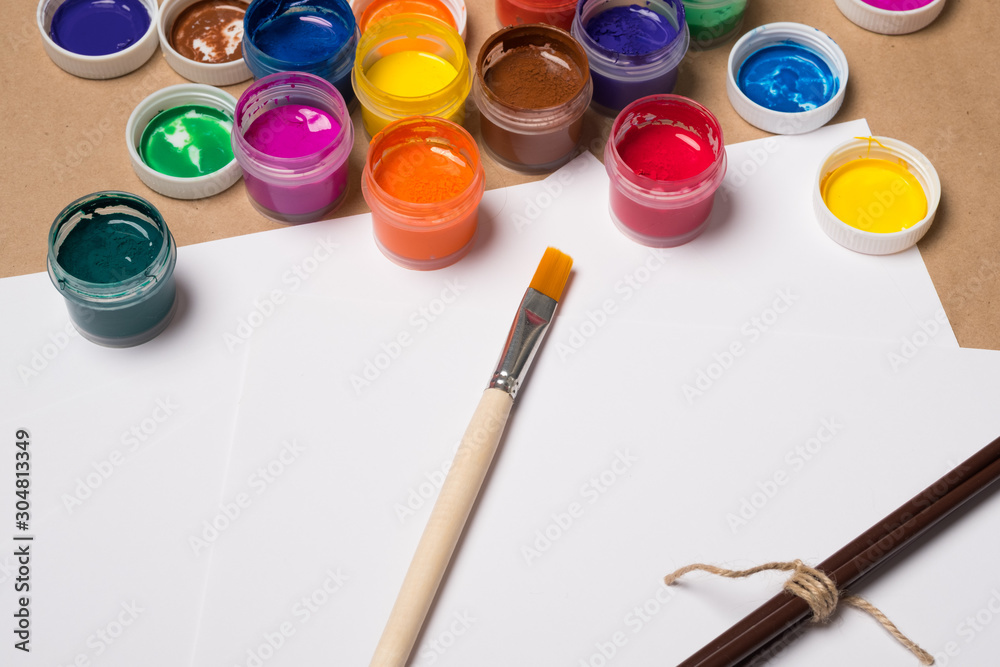 Paints for painting with brushes on a white sheet. Acrylic paints in tubes. Old paint in bottles. Paint brushes for painting and a blank white sheet of paper for text. Paints for painting with brushes on a white sheet. Acrylic paints in tubes. Old paint in bottles. Paint brushes for painting and a blank white sheet of paper for text.