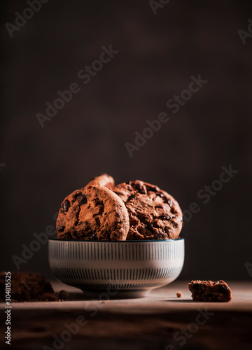 Delicious round chocolate cookies in a small porcelain dish on a brown wooden table - atmospheric low light shot with dark Background. photo