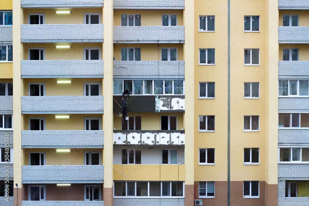 Large Building Site. Workers Building New House, install Windows, Wall Insulation, Balcony. Industrial Building Construction. Two workers perform repairs to the facade of the building at a height of