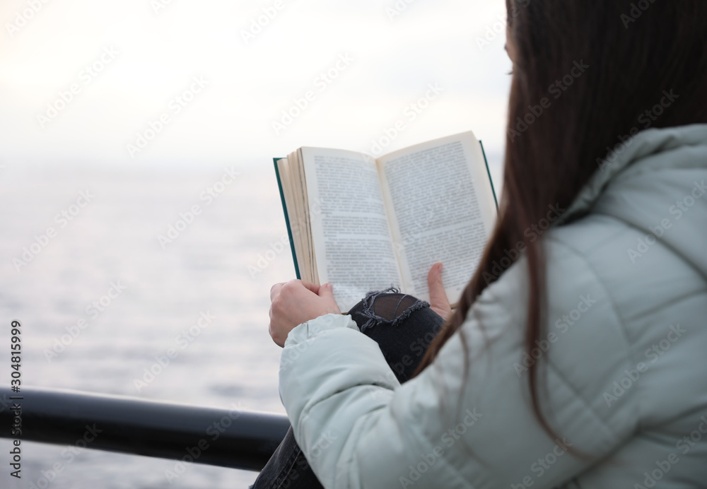 Obraz premium Woman reading book near river on cloudy day