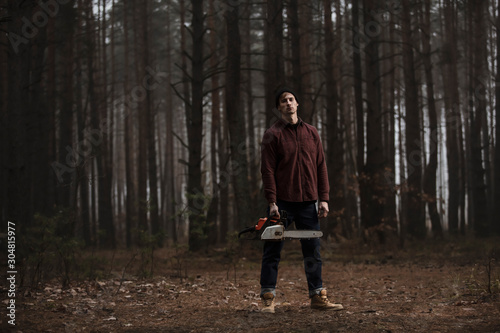 Lumberman working with chainsaw in the forest. Strong lumberjack with the chainsow in the forest.Stylish lumberman getting ready for work. Lifestyle. © nick_fedirko