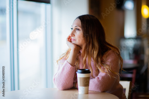White female sitting in coffee store, shop close to window. happy, beautiful, dreaming woman in sweater 