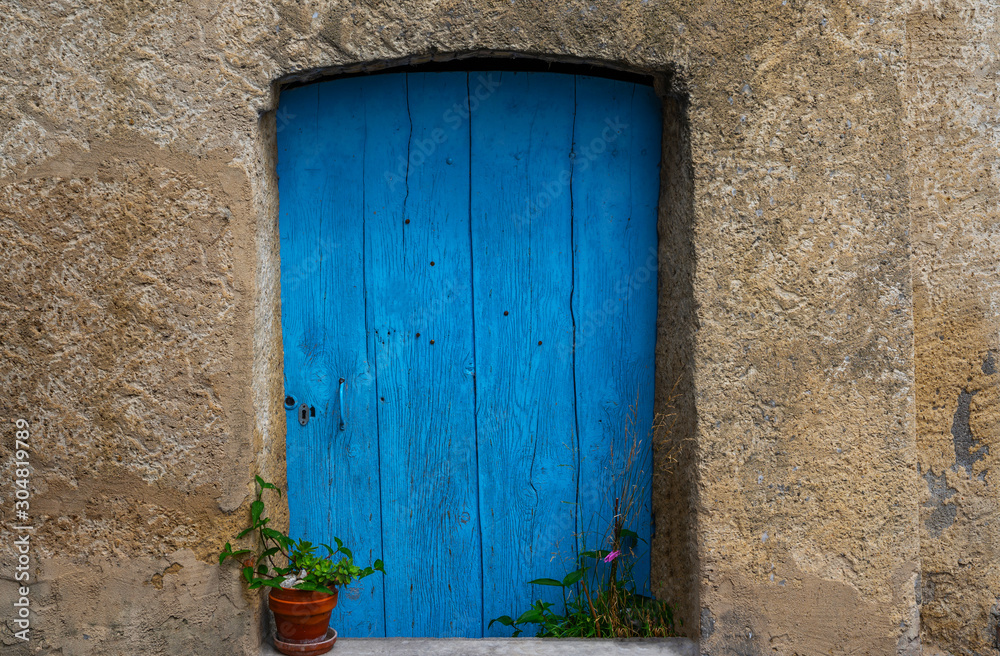 Old building in France. Wall with blue door and flower pot. Building with beautiful old architecture. Old door on old wall.