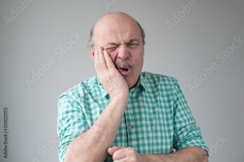 Mature spanish man feeling pain, holding his cheek with hand, suffering from bad toothache. Tooth ache concept.