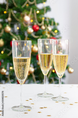 three glasses with champagne or cava on white table with christmas tree in the background
