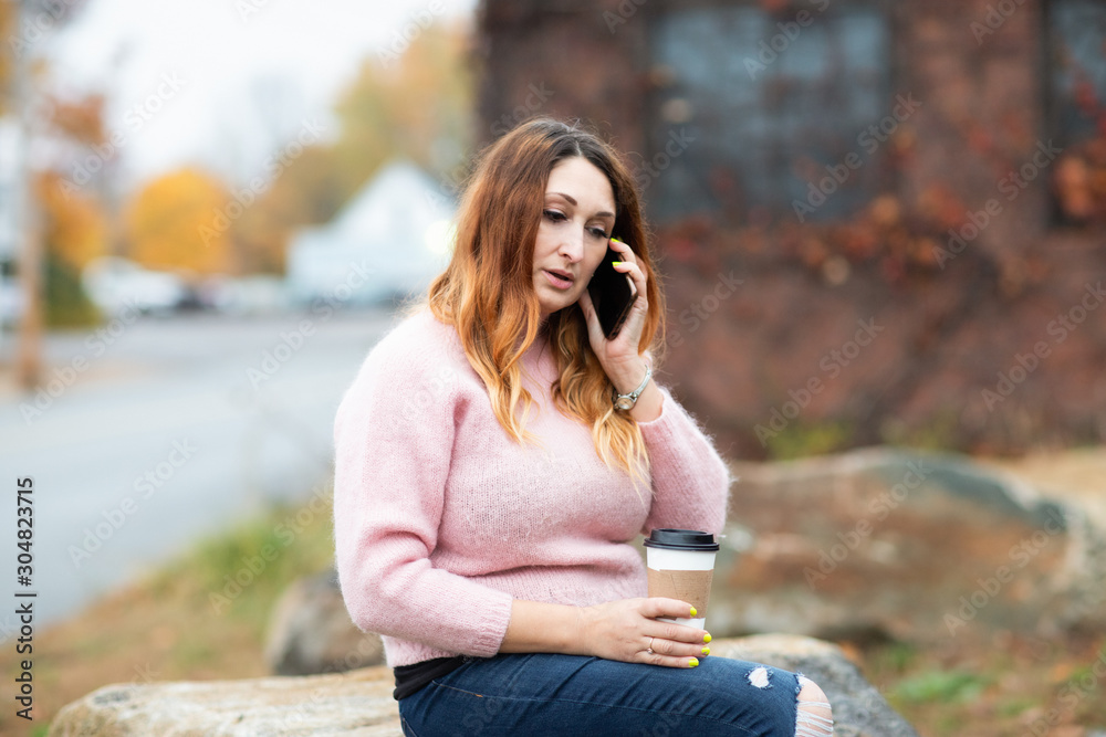 White female, Caucasian woman sitting on rock, talking on mobile phone. Autumn, Fall. White female, Caucasian woman sitting on rock, talking on mobile phone. Autumn, Fall.