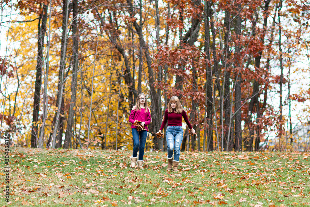 two young beautiful happy teenager girls, sisters and friends playing, running, jumping in forest. Colorful Fall, Autumn two young beautiful happy teenager girls, sisters and friends playing, running, jumping in forest. Colorful Fall, Autumn